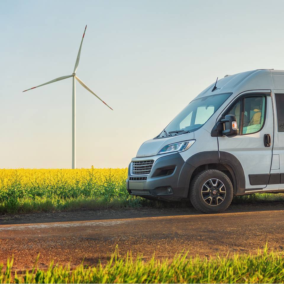 White van driving past wind turbine and field
