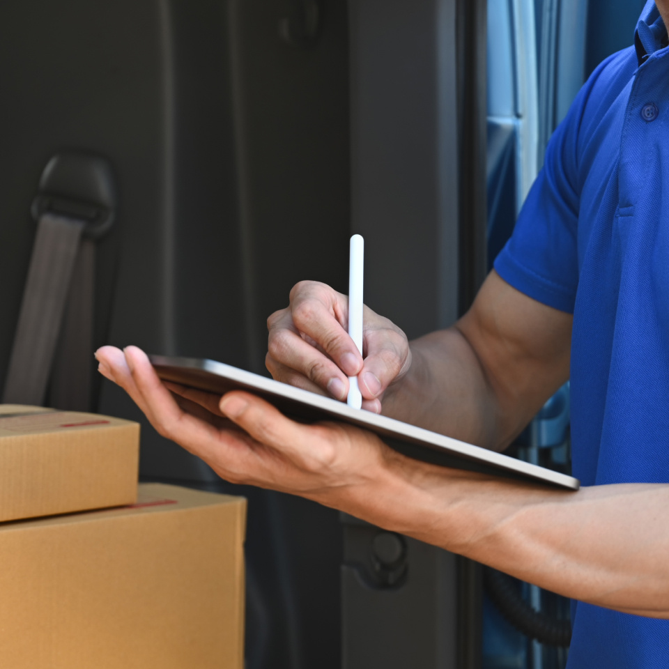 Man in blue shirt writing on tablet with parcels in van